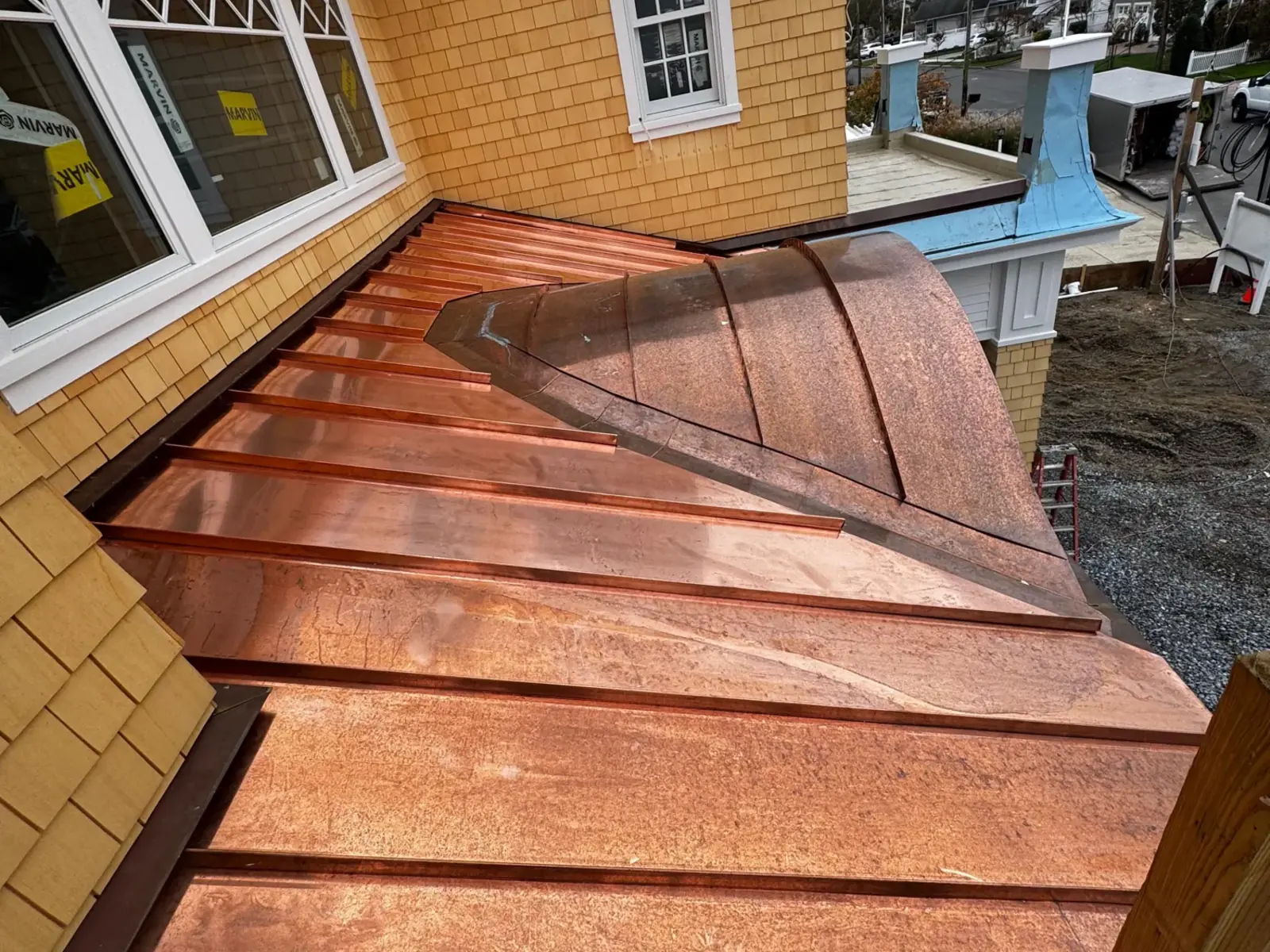Close view of a finished copper roof beside a dormer on a shingle sided house