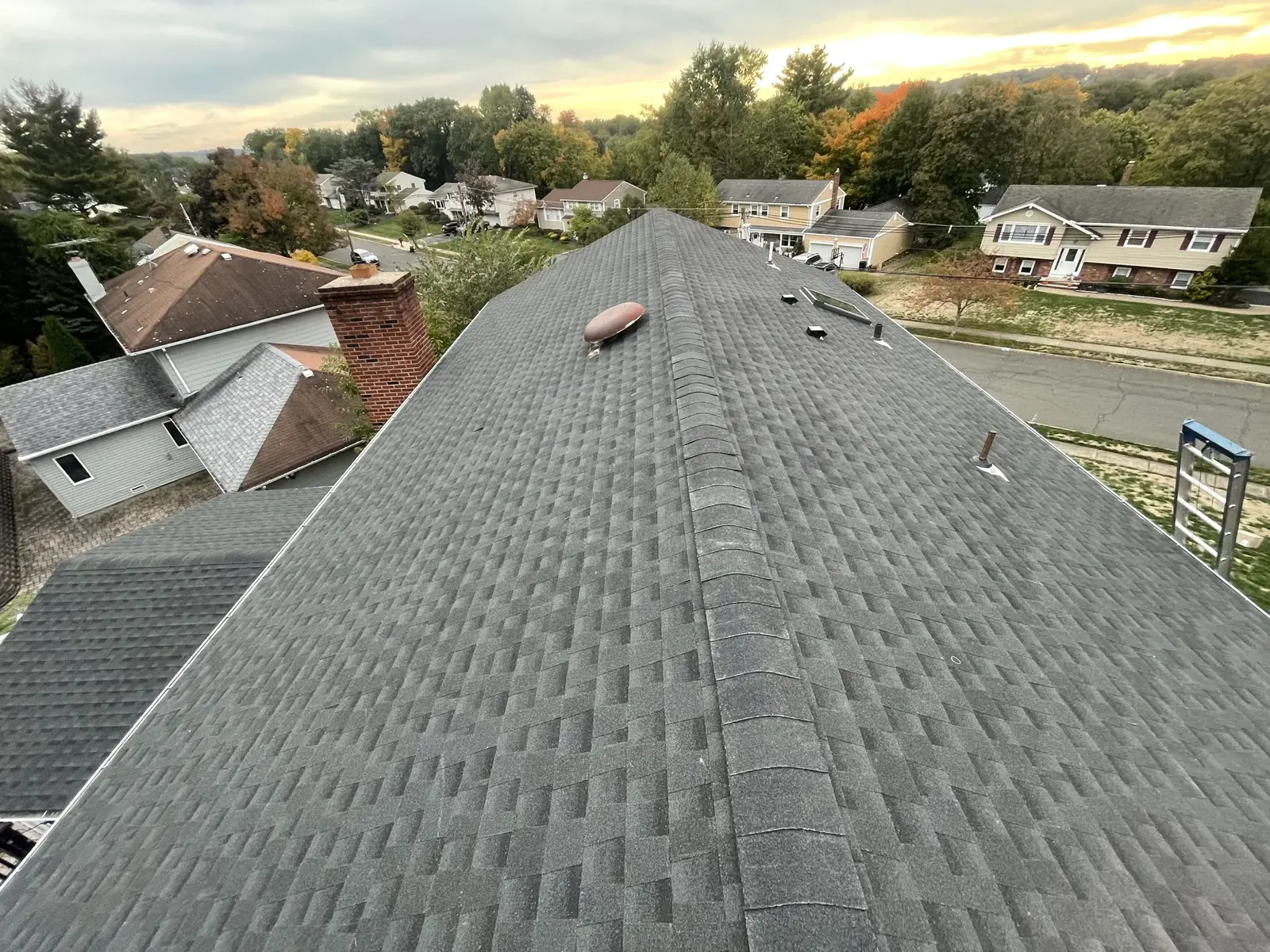 Close view of a finished grey shingle roof with an autumn neighborhood in the background
