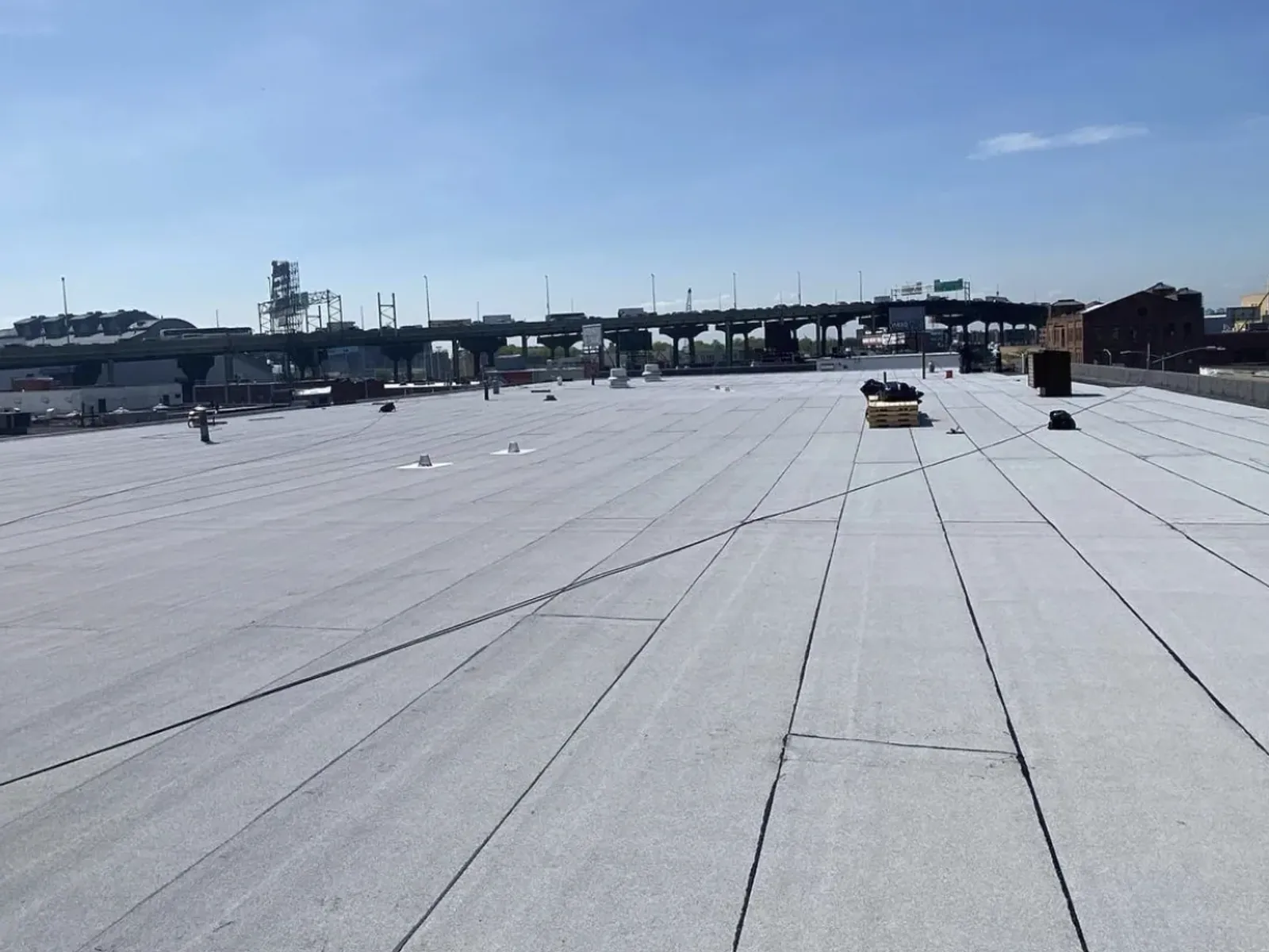 A large finished grey commercial flat roof running to the parapet, with elevated train tracks in the distance