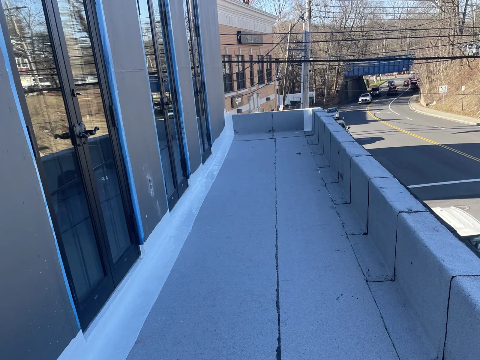 A finished light grey flat roof running between a glass wall and a parapet, with a street and traffic below