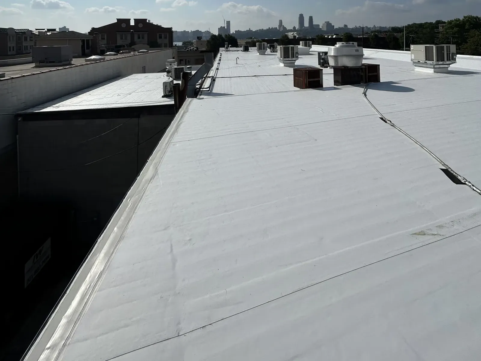 A finished white commercial flat roof with rooftop units along the ridge, stretching toward a city skyline
