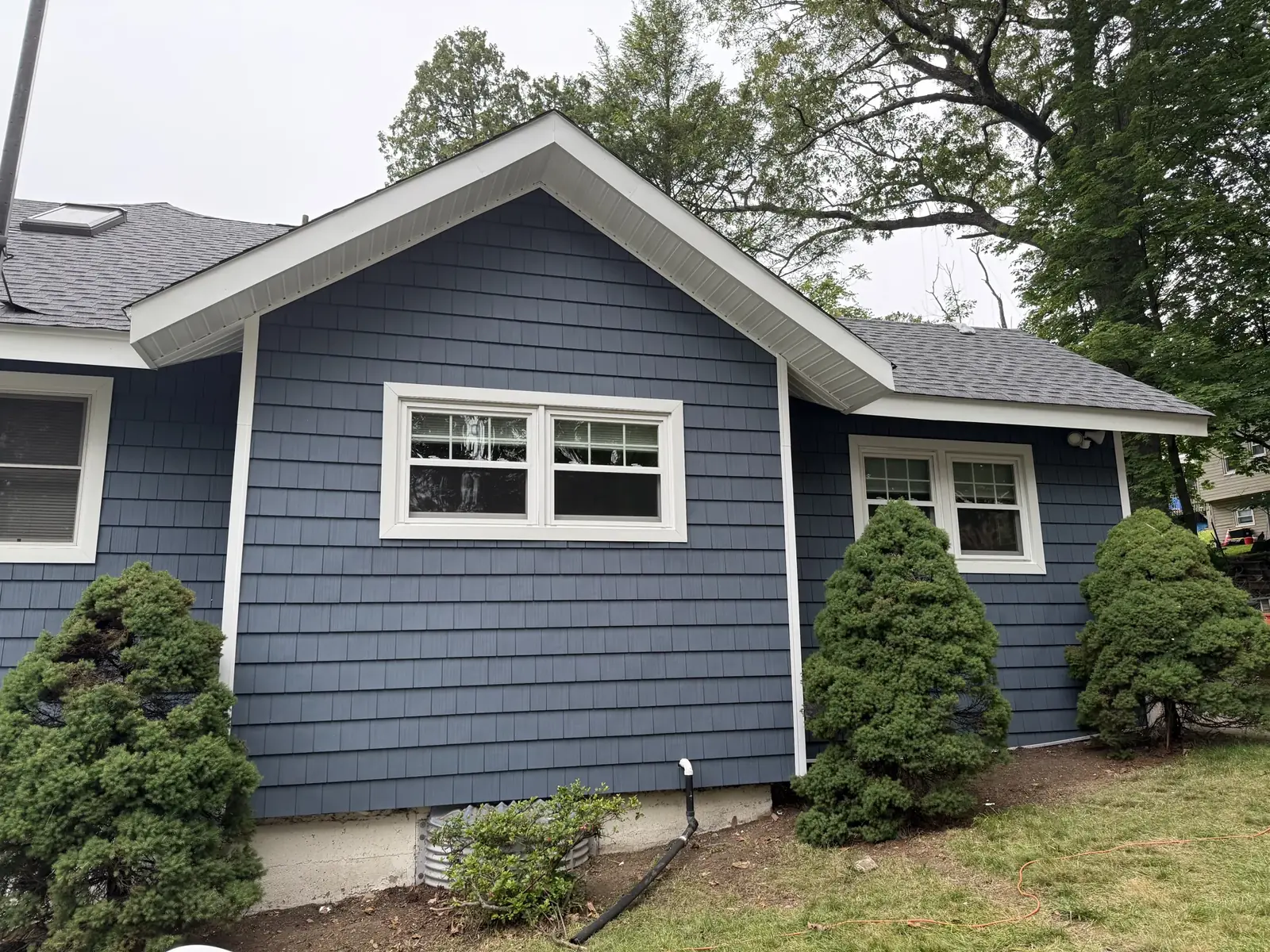 A finished blue shake style siding home, gable end with white trimmed windows
