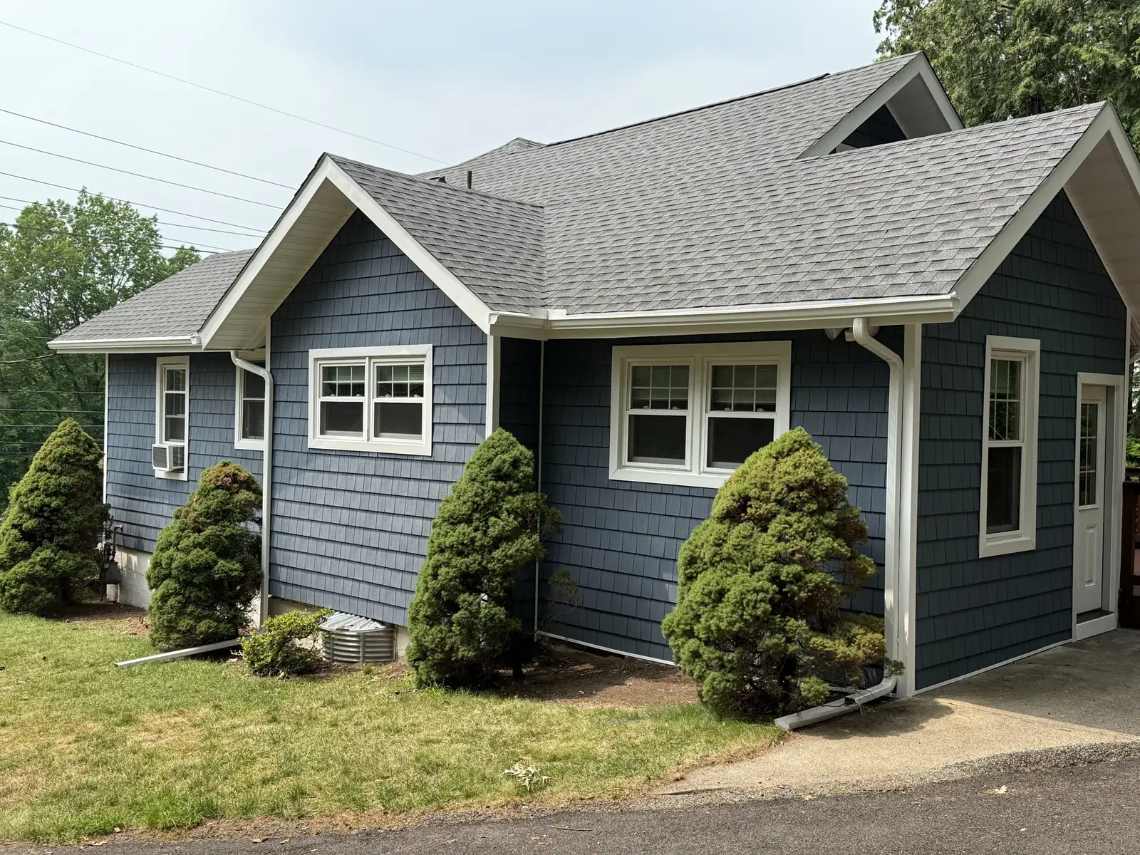 A finished blue shake style siding home, side elevation with white trim and landscaping