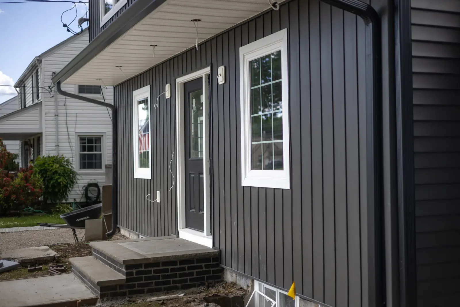 A finished dark board and batten siding entry with a black door and white trimmed windows