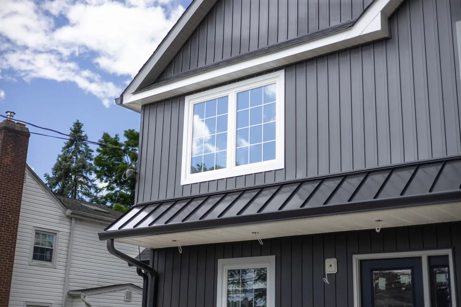 Finished dark vertical siding with white window trim and a dark standing seam overhang detail