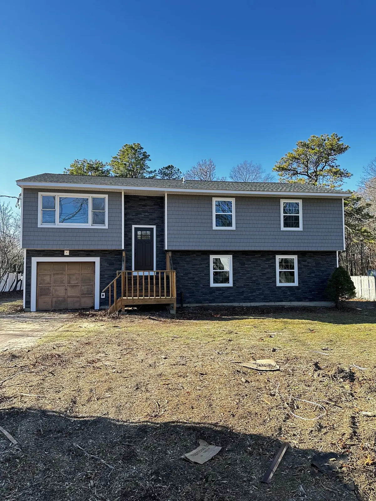 A finished grey split level home with new siding, white trim and wood porch steps