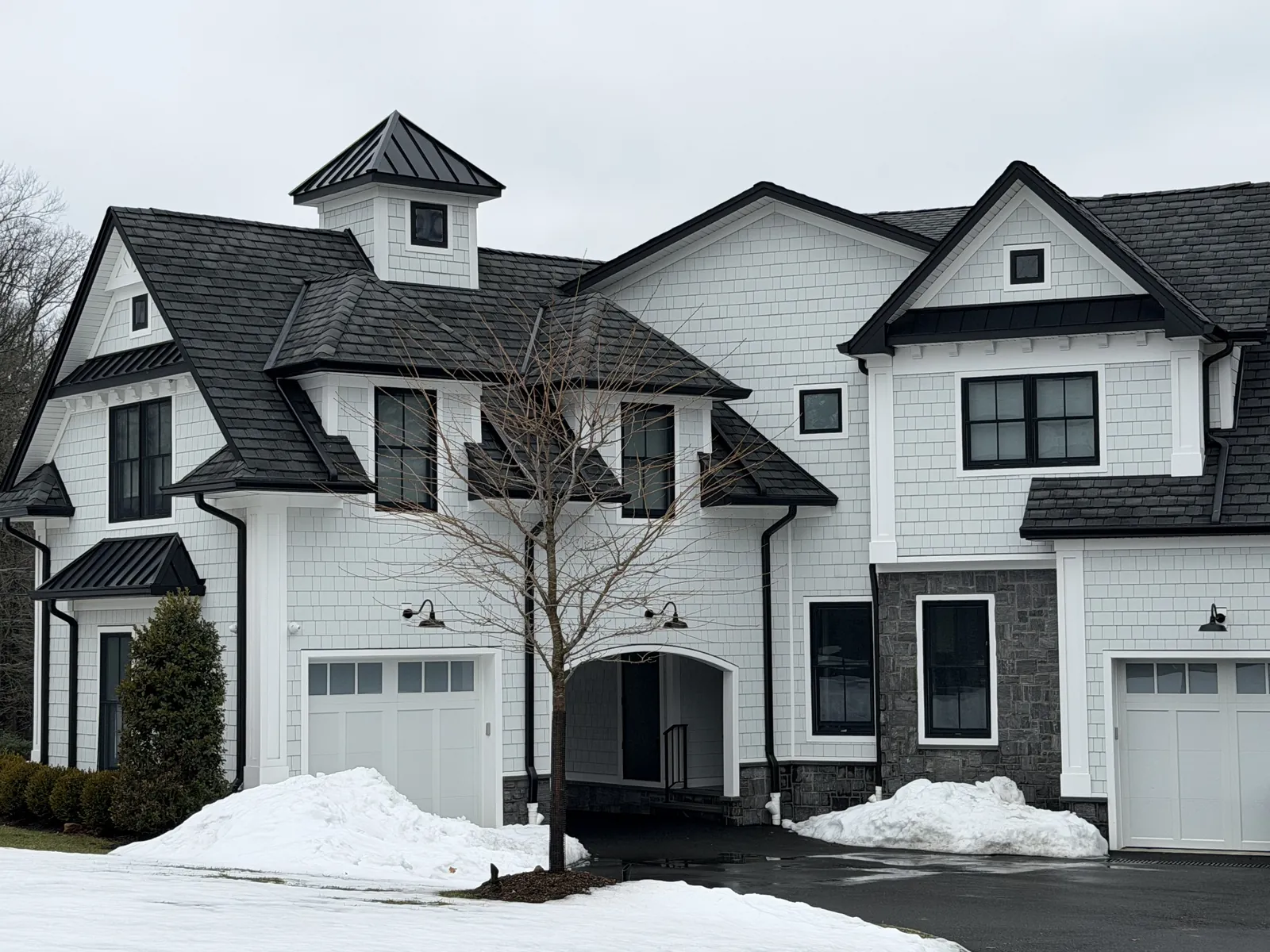 A finished dark metal roof on a white farmhouse style home with snow on the ground