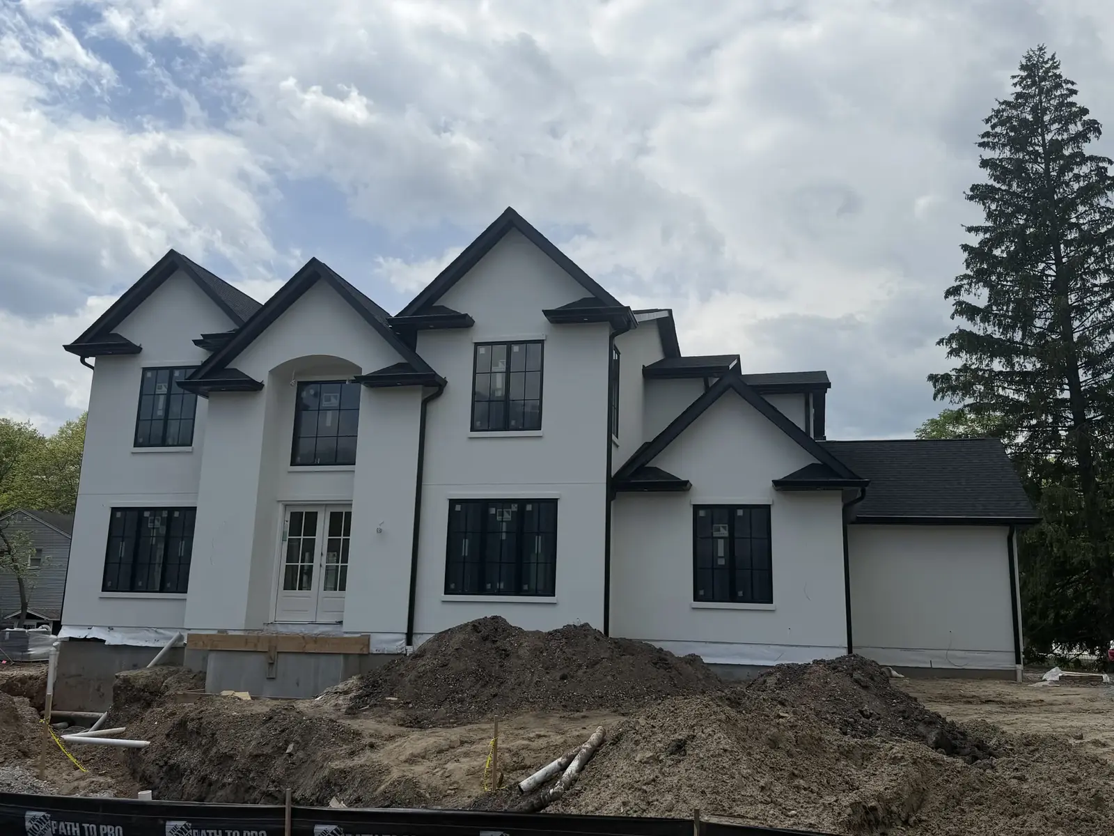 The same white stucco house from the side, black trim on the gables and windows, complete walls and roof, with soil mounds in the yard